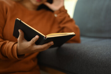 Cropped shot young woman in casual clothes reading book and spending free time at home on weekend