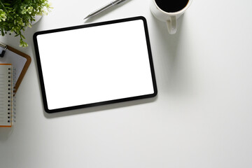 Digital tablet with empty screen, coffee cup and notepad on white table