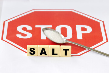 A spoon with table salt against the background of a stop sign, representing the concept of limiting salt in nutrition and products.