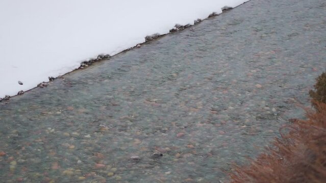 Landscape shot of river Bhaga flowing besides the snow covered river bed during the winter season at Jispa in Himachal Pradesh, India. River flows in the mountains during the winter season after snow.