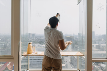 Backside view of asian Thai man wiping window glass in room apartment with city view, keep glass...