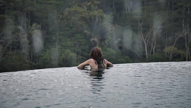 High definition slow motion footage of a woman inside infinity pool overlooking the jungle while raining in Bali, Indonesia.
Medium angle, parallax movement.