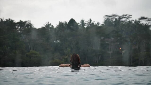 High definition slow motion footage of a woman inside infinity pool overlooking the jungle while raining in Bali, Indonesia.
Medium angle, parallax movement.