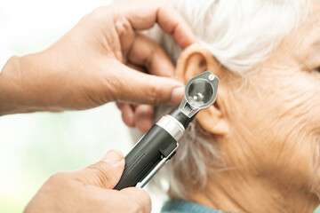 Audiologist or ENT doctor use otoscope checking ear of asian senior woman patient treating hearing loss problem.