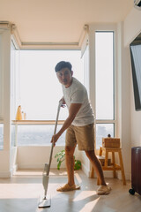 Asian Thai man using mop for cleaning floor in living room apartment, Man do household chores,...