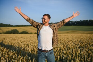 Happy farmer proudly standing in wheat field. Rich harvest of cultivated cereal crop.