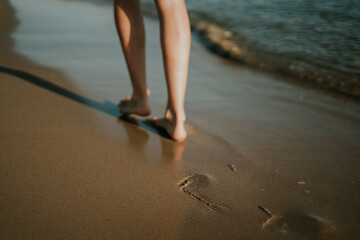 Mujer caminando por la orilla dejando sus huellas en la arena. La huella está enfocada. Puesta de...