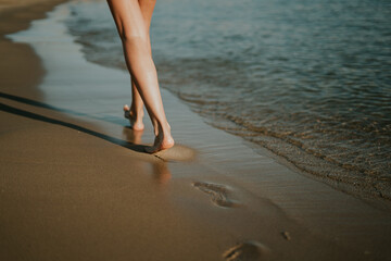 Mujer caminando por la orilla dejando sus huellas en la arena. Puesta de sol en la playa. Date un paseo para desconectar. Ondas suaves y agradables. Hermosas piernas de mujer. Relajación en verano.