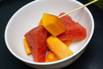 A high quality photo of fruit salad mixture of papaya and watermelon sliced and ready to eat with a stick