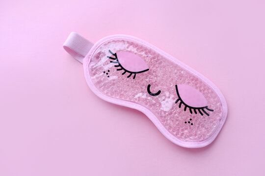 Pink sleep mask with closed eyes on it on pink background. Top view, flat layer. The concept of vivid healthy dreams.