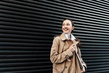 Smiling woman in trench coat looking optimistic against a striped background.