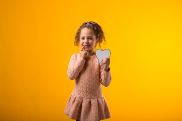 Child girl holding papercraft tooth and touching her tooth over yellow background. Dental health concept