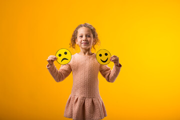 Smiling kid girl holding sad and happy emoticons in hands. Mental health, psychology and children's...