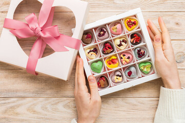 Female hands with delicious candies in box on color background