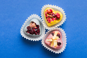 chocolate sweets in the form of a heart with fruits and nuts on a colored background. top view with space for text, holiday concept