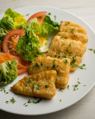 Battered white fish served with a tomato salad.