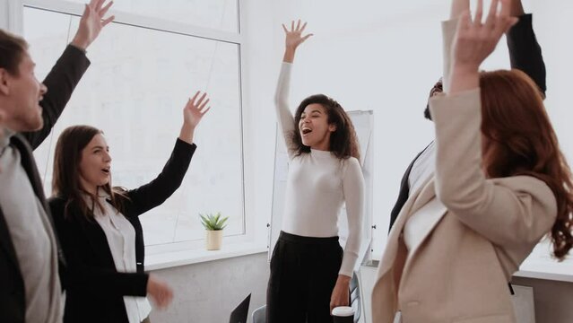 Motivated multinational team raise high fives on briefing after finding problem solution as successful brainstorm result. Happy workers unite hands above conference desk celebrate common achievement