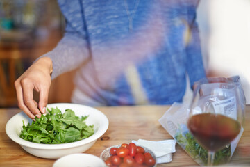 Person, cooking and prepare salad on table in kitchen closeup with wine in home for dinner. Tomato, lettuce and hands with healthy food in bowl to meal prep on counter for nutrition and diet in house