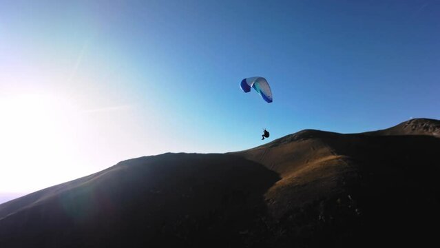 Filmed on a sports FPV quadcopter. A paragliding athlete flies on a sunny day next to a low mountain. Aerial view Adrenaline Concept, Drone Shot