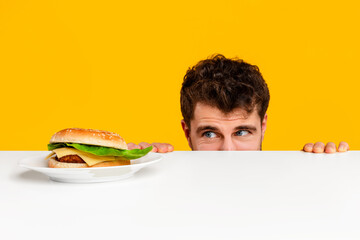 man peeking at tempting cheeseburger on plate against yellow background