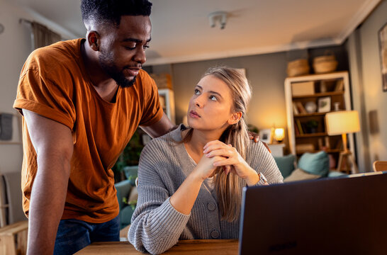 Young mixed couple using a laptop while working on their home finances.