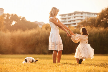 Dancing, having fun. Mother with her daughter and cute dog are on the field outdoors