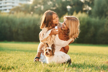Positive emotions, on the green grass. Mother with her daughter and cute dog are on the field outdoors