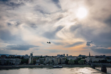 Fototapeta na wymiar An old biplane flying over the evening city of Novi Sad, Serbia against the background of amazing clouds. Chemical treatment of the territory from mosquitoes and insects