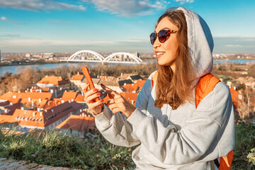 Amidst the charm of Novi Sad, a young traveler navigates the city streets, smartphone in hand, exploring its historic landmarks - obrazy, fototapety, plakaty