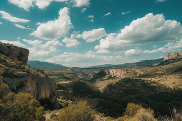 Image of cliffs overlooking a green valley. Distant hills under a partly cloudy sky. Focus on cliffs and valley. Landscape shot