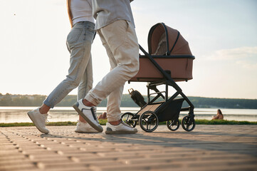 View from below of legs. A young couple with a baby pram is walking together
