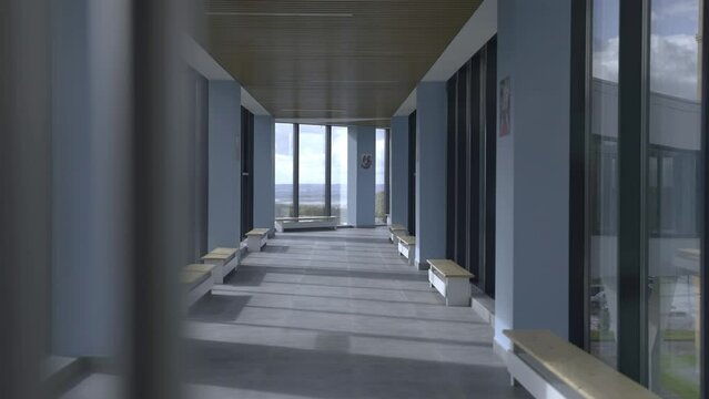 Corridor with glass walls and benches inside skyway bridge. Stylish empty hallway lit by bright sunlight. Office center interior design