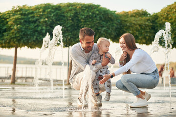 Mother and father are playing with their son in the fountains in the park