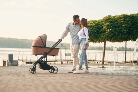 Embracing the woman by the waist. A young couple with a baby pram is walking together - Powered by Adobe