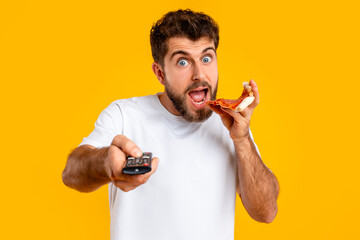 guy points remote controller savoring pizza slice on yellow backdrop
