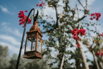 Farolillo de jardín oxidado, de fondo flores rosa fucsia. 