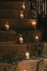 Varias velas encendidas se encuentran dentro de varios vasos de vidrio y colocadas en los diferentes escalones de una escalera de piedra. Decorado con adornos vegetales.