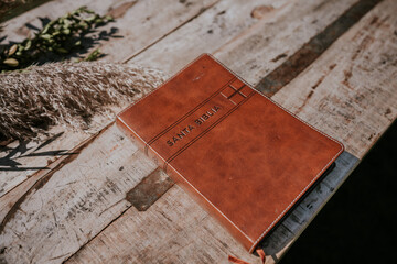 Libro de la Santa Biblia encuadernado con cuero marrón. Está apoyado sobre una mesa rústica de...