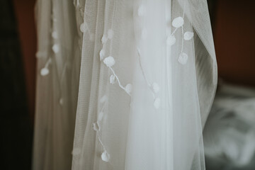 Tela de tul blanco con hojas de plantas bordadas, colgada sobre un fondo oscuro. Detalle de un vestido de novia.