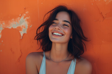 A cheerful young woman laughing with hair tousled by the wind, set against a bright orange textured...