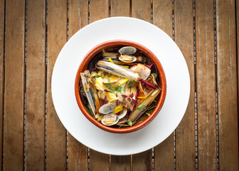Top view of mixed shellfish and fish stew with chard, tomato and hollandaise sauce in bowl in restaurant on wooden table