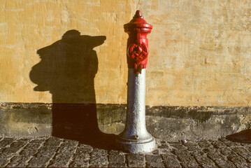 an old hydrant gives a shadow like a dog with hat