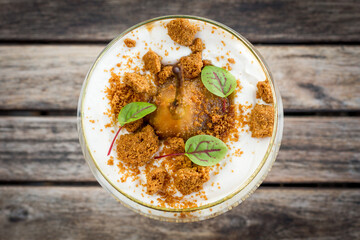 Poached pear with mascarpone and cookie crumbs in glass on wooden table