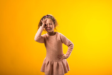 Smiling child girl looking through ok gesture over yellow background. Positive emotions concept