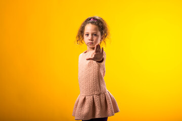 Child girl showing stop gesture on yellow background. Bulling and negative emotions concept
