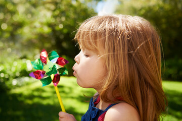 Young girl, outdoor and blowing pinwheel, garden and enjoying freedom of outside and happy. Pretty little child, backyard and summer for playing, toy and windmill for school holidays and happiness