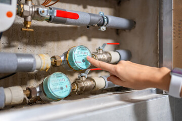 A woman's finger points to the water meters of cold and hot water consumption in real apartments, Europe