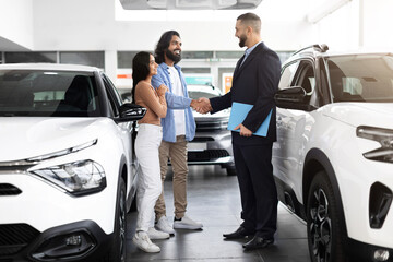 Car advisor stands discussing financing options with interested indian couple