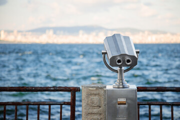 Public binoculars on the seaside promenade overlooking a distant city