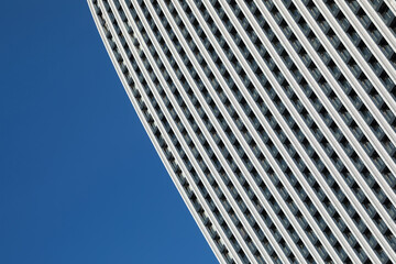 A minimalistic photo of a part of a modern building with repetitive pattern on its exterior stands out against the clear blue sky